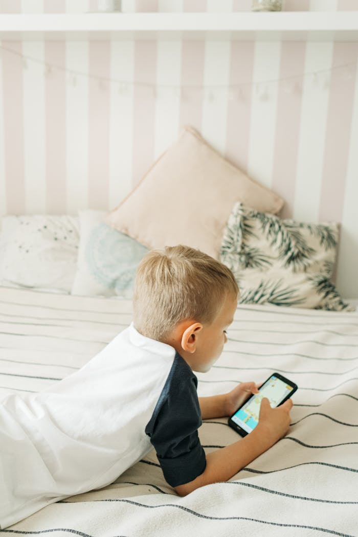 Young boy lying on bed, playing games on his smartphone in a cozy bedroom setting.